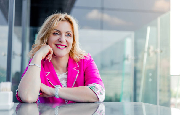 Successful woman entrepreneur in a magenta jacket posing on the terrace of a cafe in a business center. Business woman representation concept - Photo, Image
