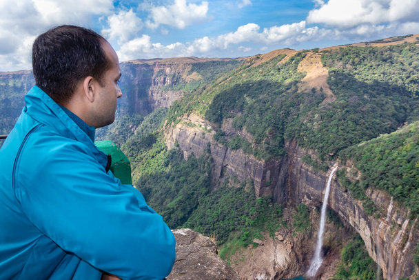 young man watching waterfall streams falling from mountain top covered with green forests at day image is taken at Nohkalikai Falls cherrapunji meghalaya india. - Photo, Image
