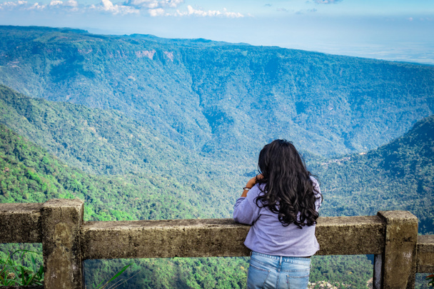 młoda dziewczyna obserwująca pasmo górskie z jasnym błękitnym niebem po południu od płaskiego kąta obraz jest robiony na siedmiu siostrzanym wodospadzie cherrapunji meghalaya india. - Zdjęcie, obraz