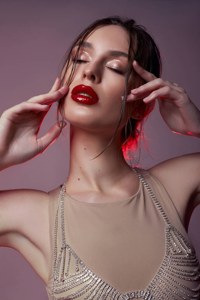 Beauty sexy woman in beige bodysuit, bra jewel jewelry made of rhinestones. Perfect body woman, bright red makeup. Beautiful curled hair - Фото, зображення