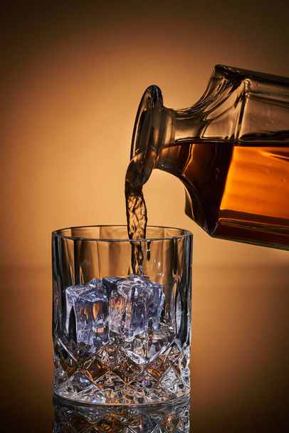 Pouring whiskey in a glass over ice cubes - Foto, Imagem