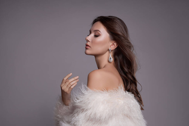 Beauty art portrait of a beautiful woman with long hair, white fur coat with long faux fur. Beautiful earrings in a woman's ears. Hairstyle, hair styling - Foto, Imagem