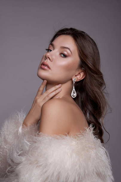 Beauty art portrait of a beautiful woman with long hair, white fur coat with long faux fur. Beautiful earrings in a woman's ears. Hairstyle, hair styling - Photo, image