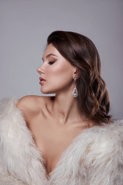 Beauty art portrait of a beautiful woman with long hair, white fur coat with long faux fur. Beautiful earrings in a woman's ears. Hairstyle, hair styling - Фото, изображение