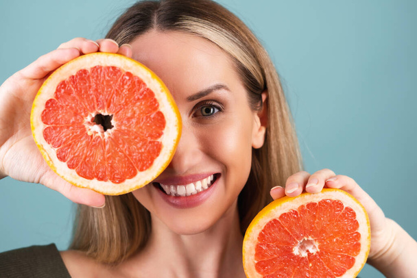 Közelkép egy félmeztelen nőről tökéletes bőrrel és természetes sminkkel, teljesen meztelen ajkakkal, friss C-vitamin grapefruitot tartva - Fotó, kép