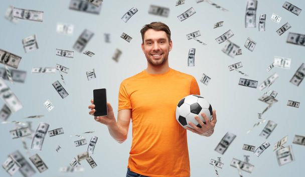 hombre con teléfono inteligente y pelota de fútbol sobre el dinero - Foto, Imagen