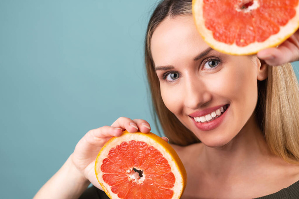 Закрытый портрет безтонной женщины с идеальной кожей и естественным макияжем, полностью обнаженными губами, со свежим цитрусовым витамином С грейпфрутом - Фото, изображение