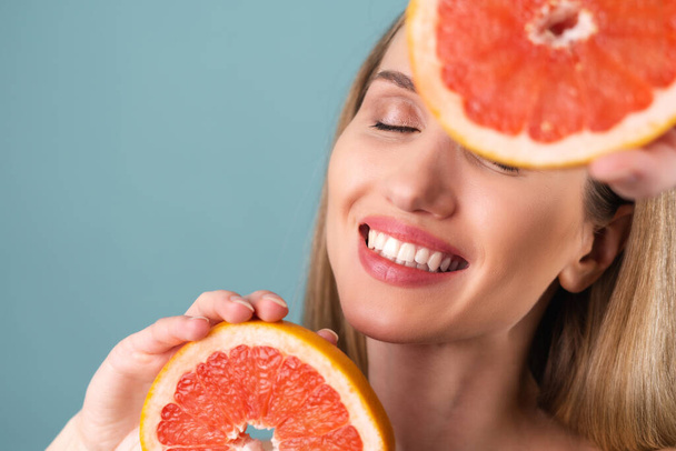 Detailní portrét ženy nahoře bez s perfektní pletí a přirozeným make-upem, plné nahé rty, držící čerstvý citrusový vitamin C grapefruit - Fotografie, Obrázek
