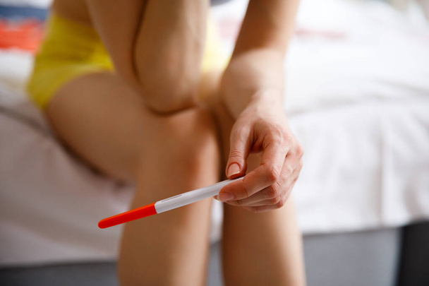 A sad young woman holds a pregnancy test in her hand. The concept of unwanted pregnancy. - Photo, Image