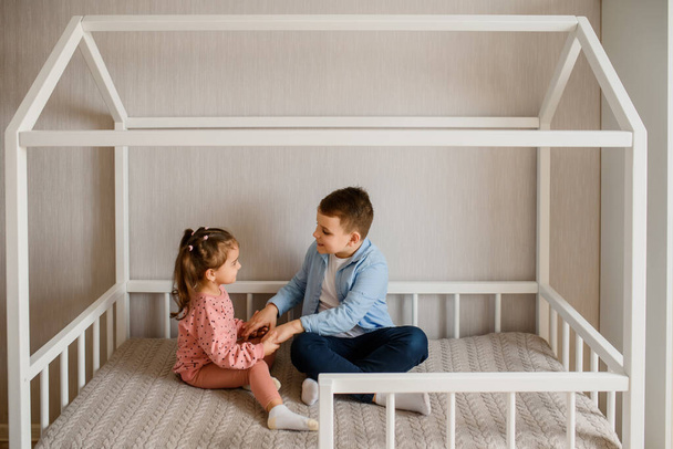 Two Children brother and sister are sitting in a Montessori bed and looking at each other. Bed for kids in a house shape - Фото, зображення