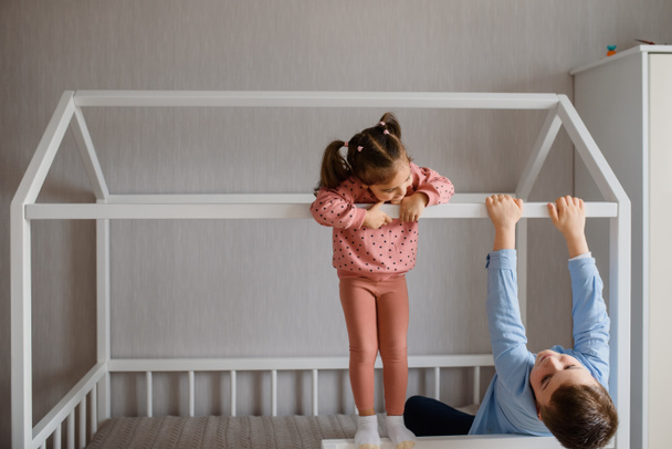 Dos niños hermano y hermana están sentados en una cama Montessori y mirando el uno al otro y jugando. Cama para niños en forma de casa - Foto, Imagen
