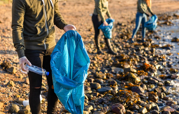 Κοντινό πλάνο του ανθρώπου συλλέγει σκουπίδια σε τσάντα με την ομάδα των εθελοντών την ηλιόλουστη μέρα - Φωτογραφία, εικόνα