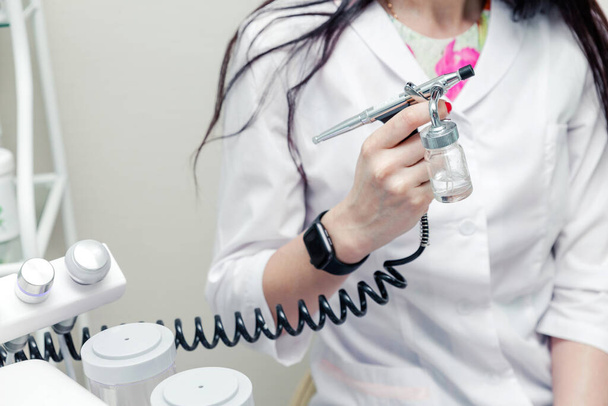 Beautician posing next to a beauty machine and an oxygen injection gun in her hand. Horizontal photo - Photo, Image