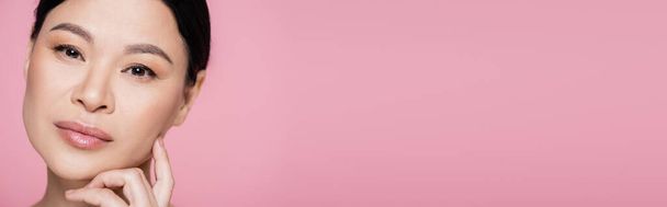 Азійська жінка з косметикою дивиться на камеру ізольовану на рожевому плакаті.  - Фото, зображення