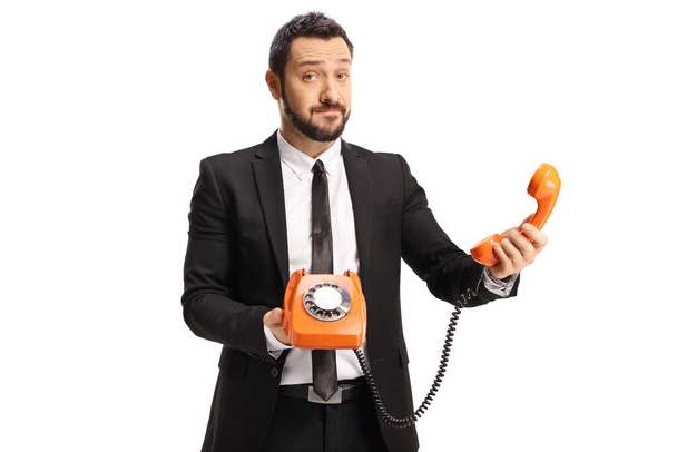 Confused businessman holding an orange rotary phone isolated on white background - Foto, Bild