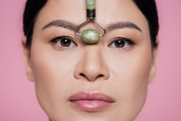 Vue rapprochée du rouleau de jade près du nez de la femme asiatique isolée sur rose  - Photo, image