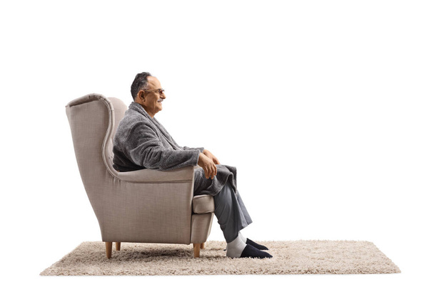 Profile shot of a mature man in a bathrobe sitting in an armchair isolated on white background - Photo, Image