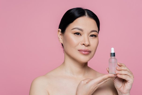 Asian woman with naked shoulders holding serum isolated on pink  - Fotografie, Obrázek