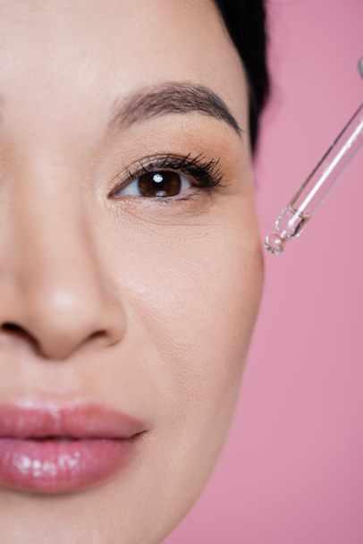 Cropped view of asian woman applying serum on cheek isolated on pink  - Фото, изображение