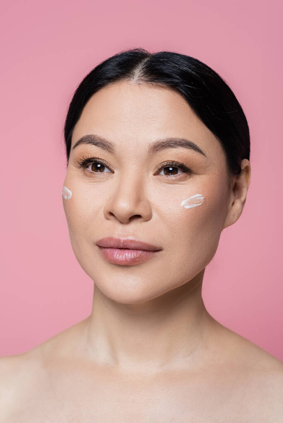 Asian woman with naked shoulders and cream on face isolated on pink  - Foto, Bild