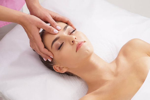 Beautiful, young and healthy woman having face massage in spa salon. Hands of professinal masseur. Spa, health and healing concept. - Fotó, kép