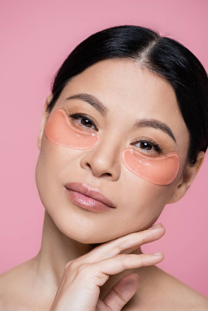 Porträt einer asiatischen Frau mit Augenklappen, die isoliert auf rosa Kamera schaut  - Foto, Bild