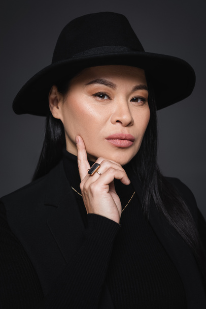 Портрет модної азійської жінки в федора капелюх дивиться на камеру ізольовану на темно-сірому - Фото, зображення