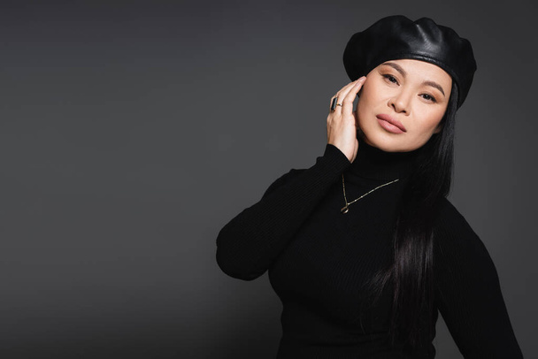 Asian model in necklace and beret looking at camera isolated on dark grey - Fotografie, Obrázek
