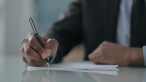 Gros plan des mains d'un homme d'affaires africain écrivant sur papier - Séquence, vidéo