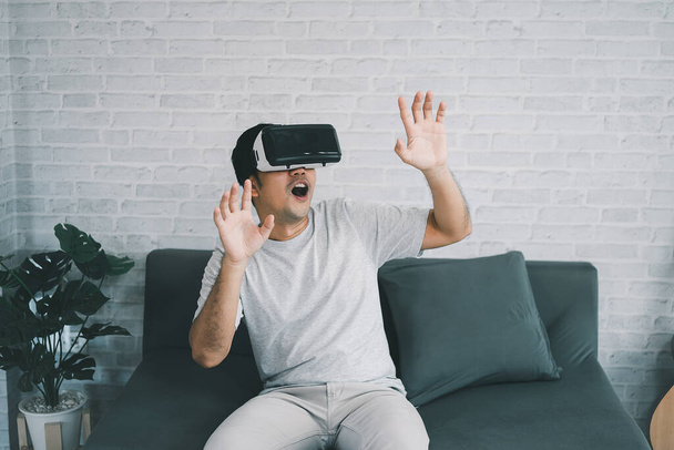 Asian man play VR game for entertain at home, asian man joyful  in house on holiday. Happy man playing metaverse VR technology concept. - 写真・画像