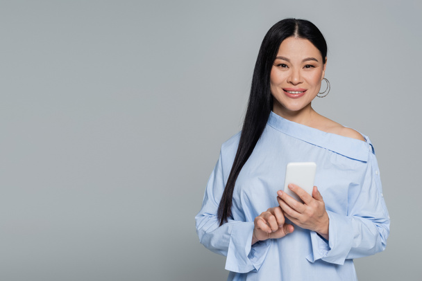 Positivo asiático mujer en blusa usando móvil aislado en gris  - Foto, imagen