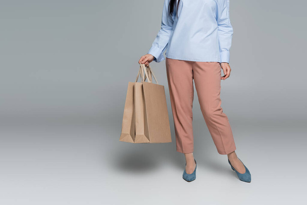 Cropped view of stylish woman holding shopping bags on grey background  - Foto, Imagem