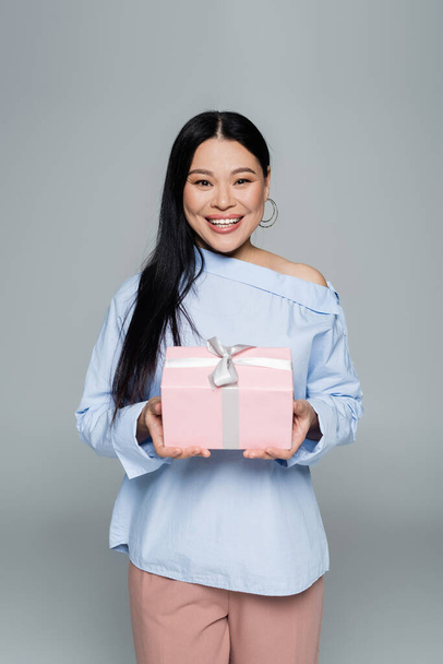 Joyful asian woman holding present isolated on grey  - Foto, Imagem