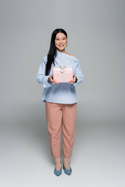 Cheerful asian model holding present on grey background  - Фото, зображення