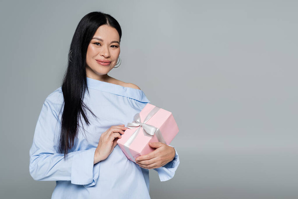 Asian woman in blue blouse holding present isolated on grey  - Foto, Bild