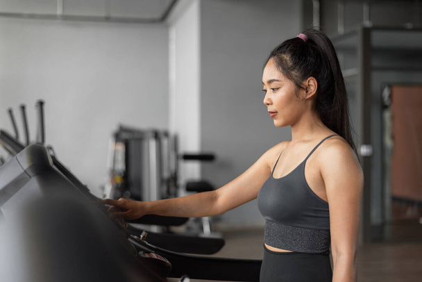 Asian woman exercises in fitness. Young healthy woman in sportswear is running on a treadmill in gym. - Fotó, kép