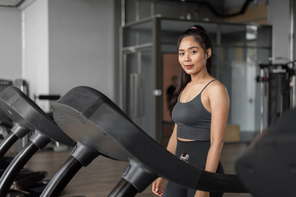 Ázsiai nő tornázik fitnesz órán. Fiatal, egészséges nő sportruházatban futkározik egy futópadon az edzőteremben.. - Fotó, kép