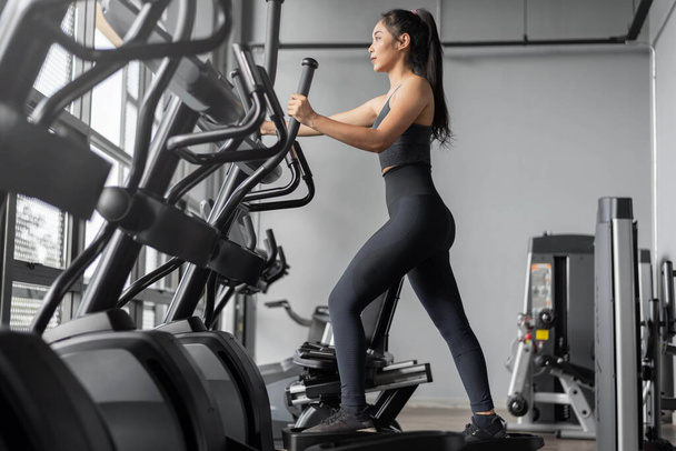 Femme asiatique fait des exercices de fitness. Jeune femme en bonne santé en vêtements de sport est des exercices cardio dans la salle de gym. - Photo, image