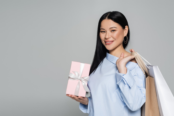 Positief Aziatisch model met aankopen en geschenken geïsoleerd op grijs  - Foto, afbeelding
