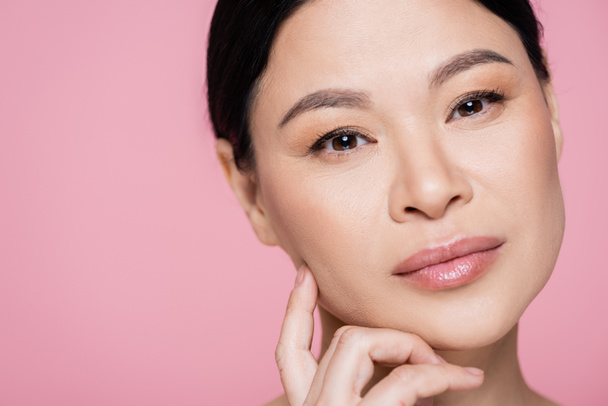 Portrait of brunette asian woman with makeup looking at camera isolated on pink  - Photo, Image