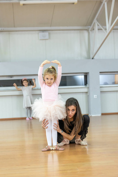 Young trainer of the ballet school helps young ballerinas perform different choreographic exercises in studio. Ballet class for kids and toddlers - Foto, Imagem