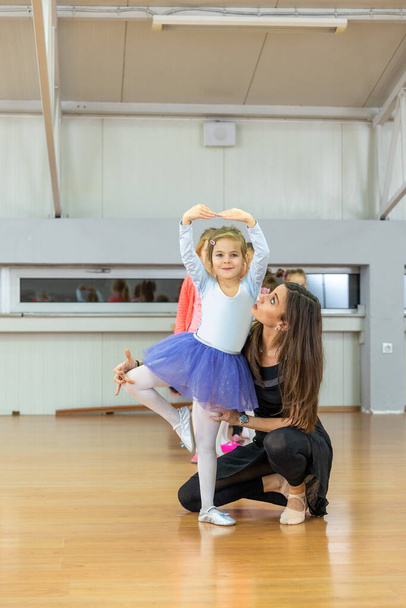 Young trainer of the ballet school helps young ballerinas perform different choreographic exercises in studio. Ballet class for kids and toddlers - Foto, Imagem