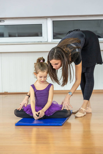 Young trainer of the ballet school helps young ballerinas perform different choreographic exercises in studio. Ballet class for kids and toddlers - Fotó, kép
