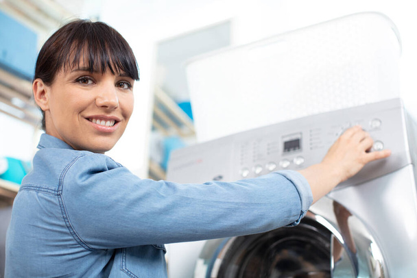 woman pressing button of washing machine in kitchen - Foto, imagen