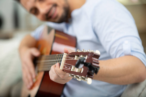 pretty young man playing guitar while sitting on sofa - Φωτογραφία, εικόνα
