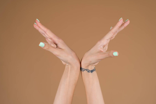 Graceful female hands with thin long fingers and mint turquoise manicure on a beige background - Photo, Image