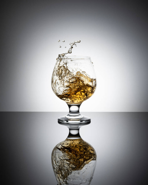 Splash of cognac in glass isolated on a light background. - Фото, изображение