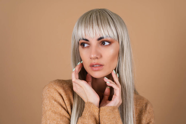 Blonde girl with bangs and brown daytime make-up in a sweater on beige background sensual fashion portrait - Foto, Bild