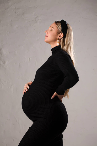 Portrait of a young beautiful pregnant woman in a black dress - Фото, изображение