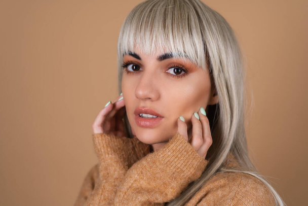 Blonde girl with bangs and brown daytime make-up in a sweater on beige background sensual fashion portrait - Photo, Image